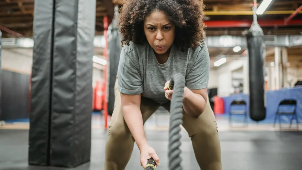 Woman performing anaerobic workout with battle ropes in gym