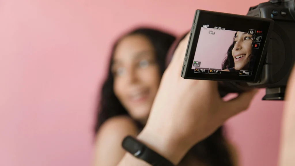 Camera viewfinder with focus grid showing a young woman posing against a pink background