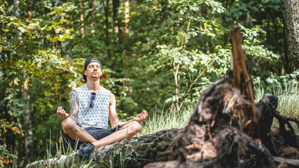 Man meditating on a tree log outdoors - how to improve concentration.