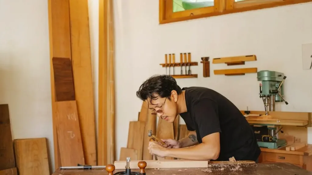 Concentrated Asian craftsman performing concentration exercises while chiseling a wooden plank in a joinery