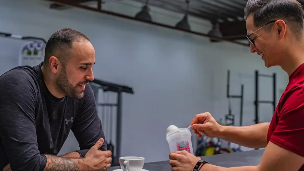 Friends making protein shake after workout, discussing if it's best to drink before or after exercise.