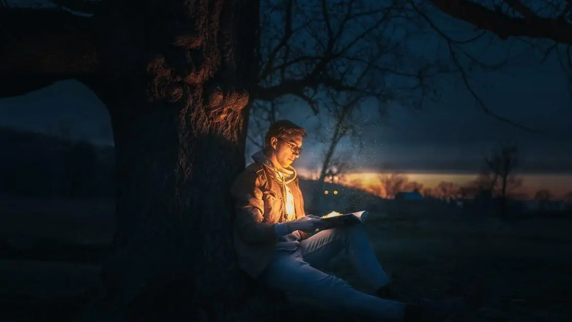 Man reading a book under a tree at night to boost cognitive function