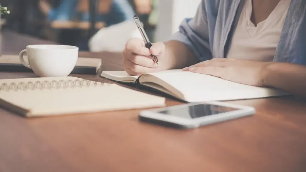 Woman jotting down notes beside a teacup and tablet, illustrating how to improve working memory.