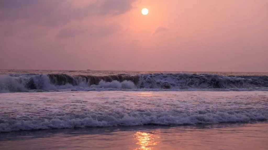 Sunset over the ocean, waves crashing.