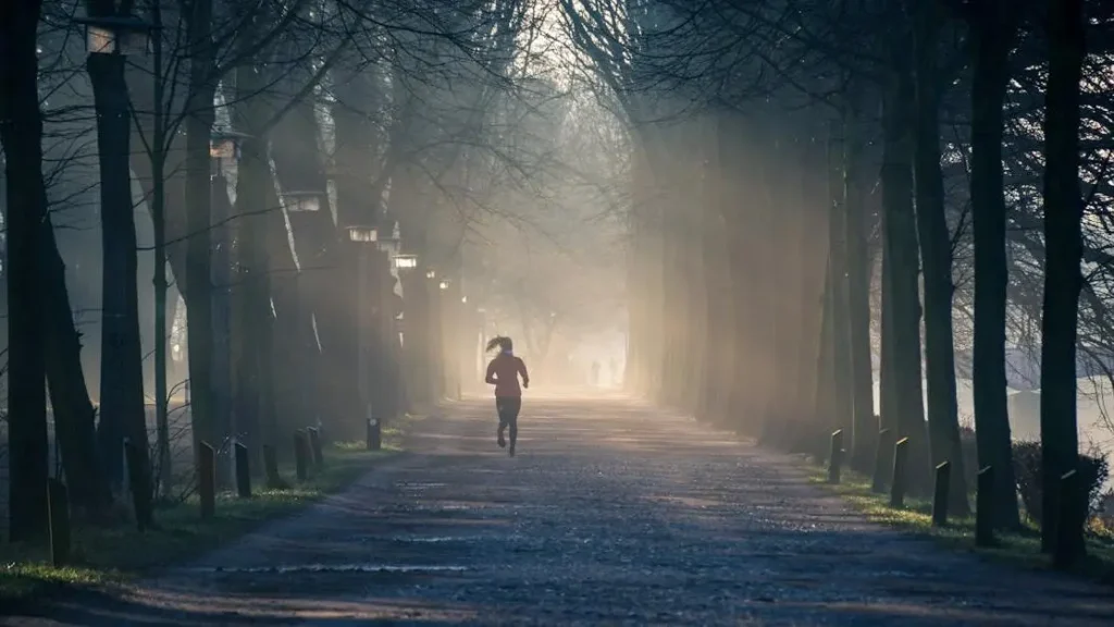 Running person on street lined with tall trees, illustrating morning exercise.